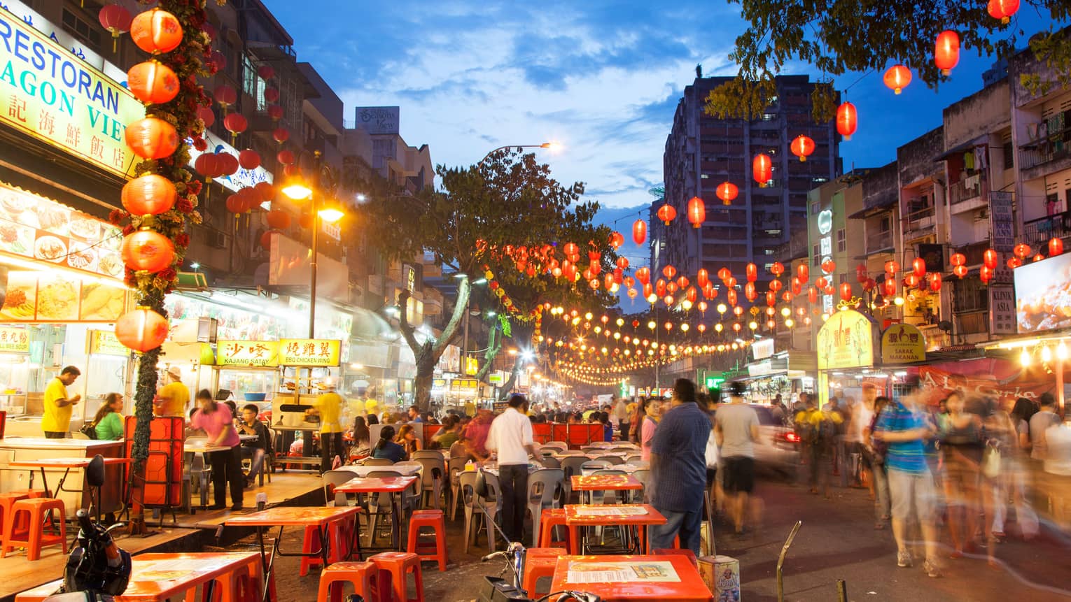 Red lanterns, lights hang over Jalan Alor Food Street tables, crowds at dusk