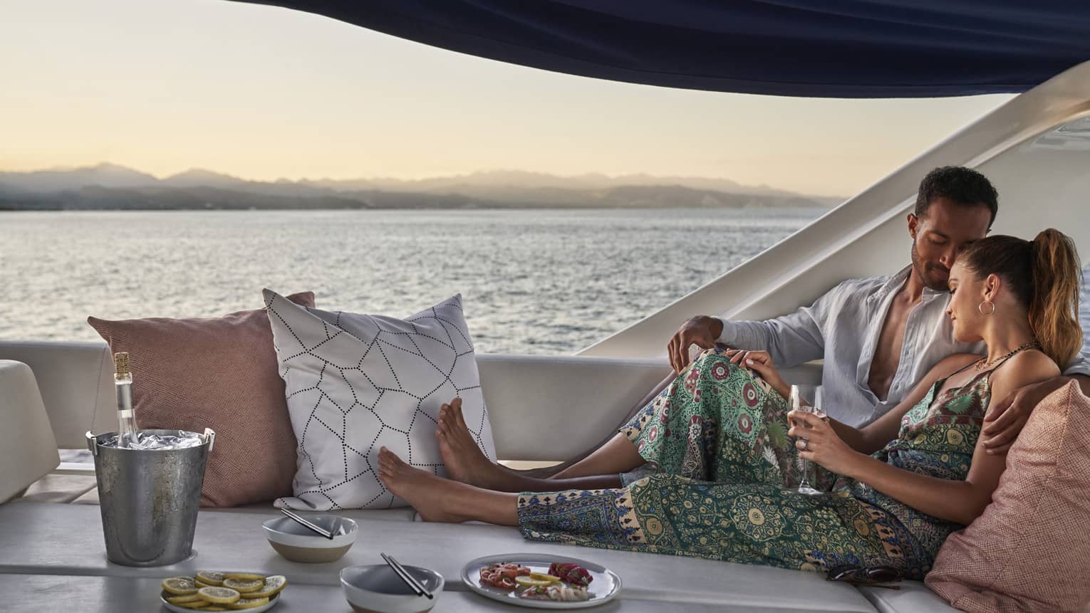 Couple relaxes with food and drinks on sofa on yacht