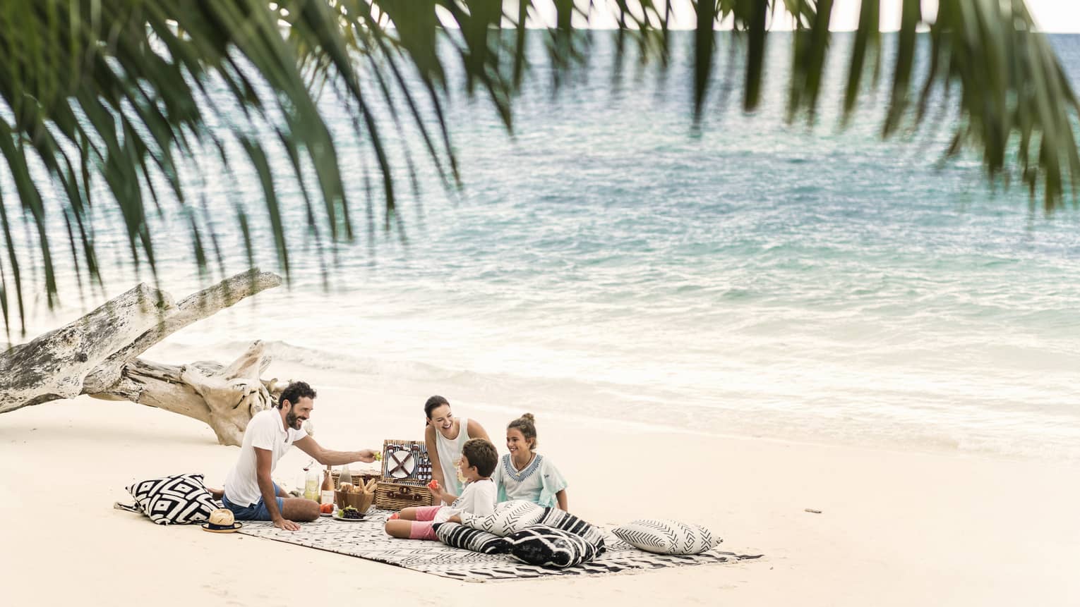 A man, woman and two children picnic on the beach just a couple feet away from the ocean. 