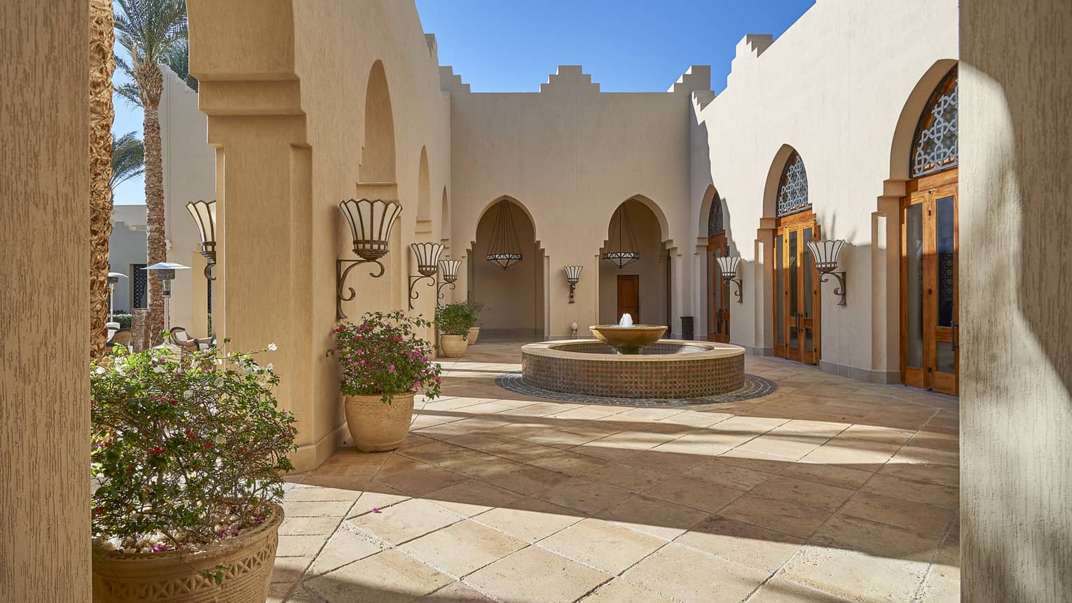 Small fountain in sunny courtyard surrounded by white stone walls, planters