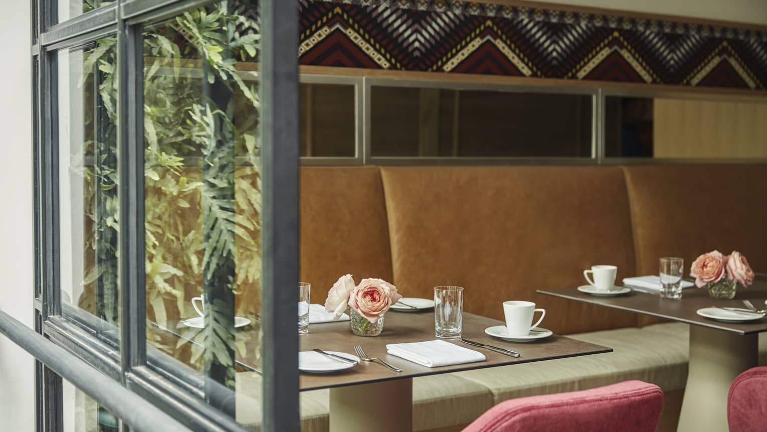 A dining booth with a brown couch and red chairs, and roses set on the table.