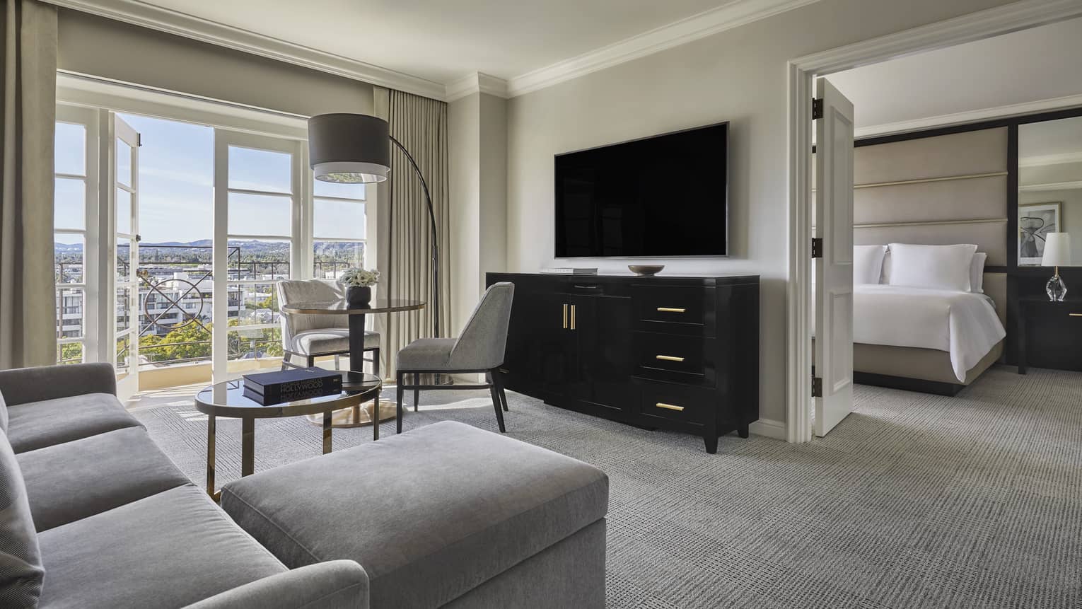 Living area with grey sofa, TV, small table with two chairs, french doors opening to bedroom