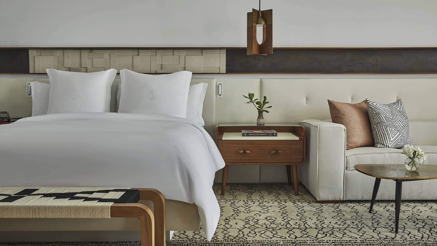 Four Seasons hotel bed, positioned next to wooden side table and sitting area with sofa