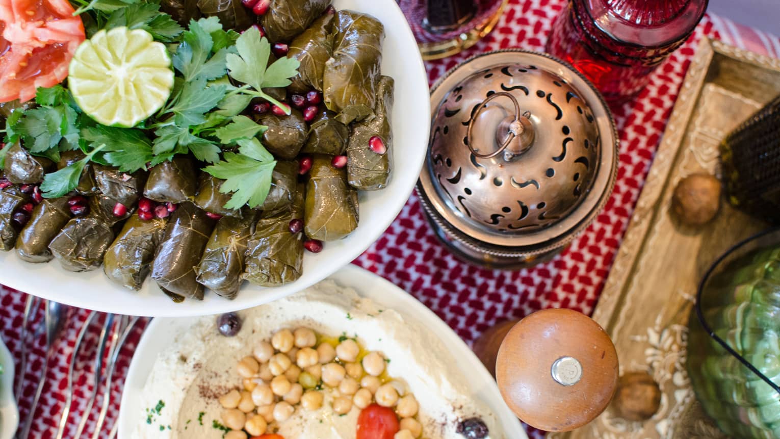 Grape leaf-wrapped appetizers on platter with fresh parsley, lemon, chickpea hummus