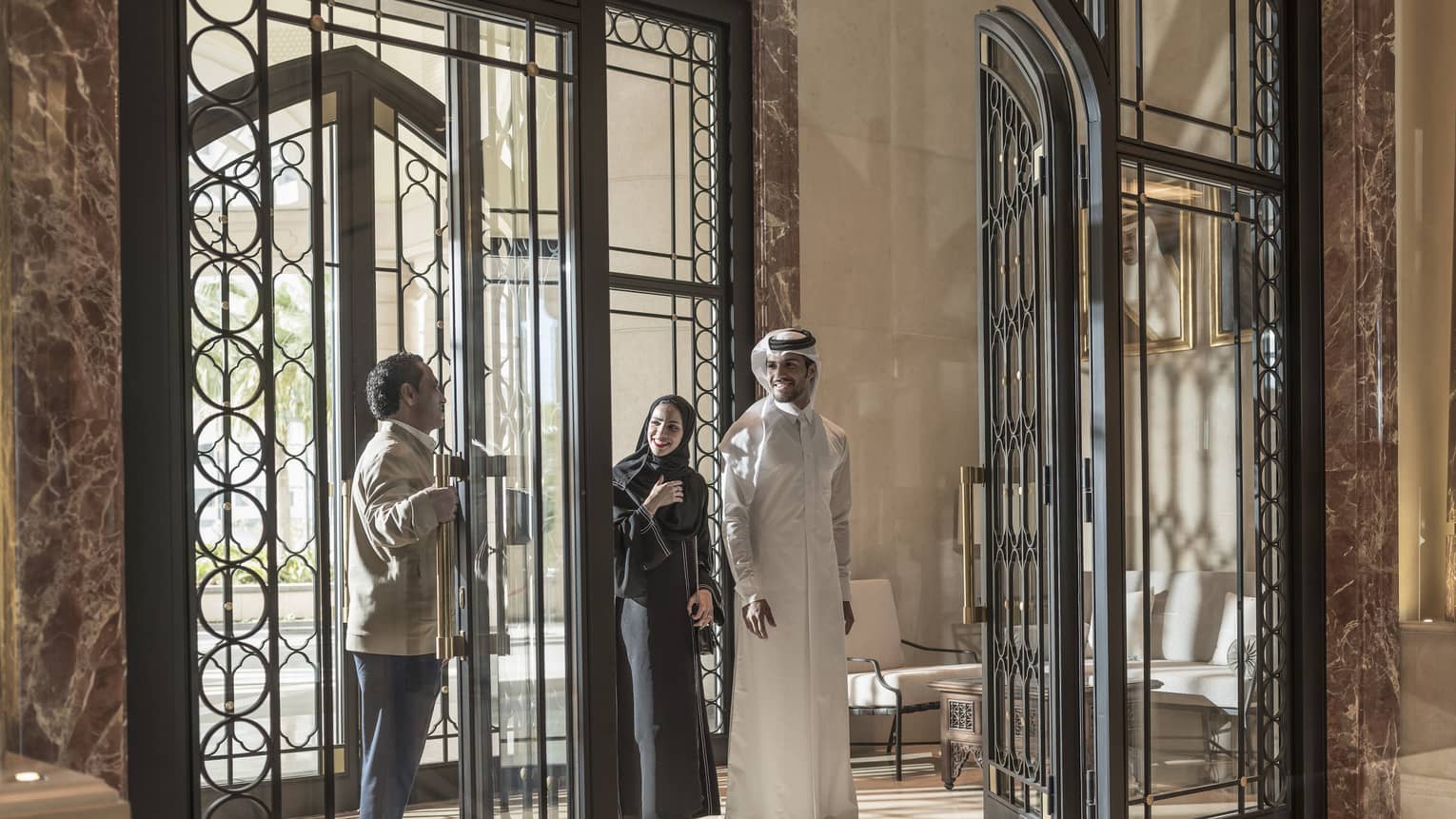 A man in a Four Seasons uniform opens the wrought iron doors for a couple. 