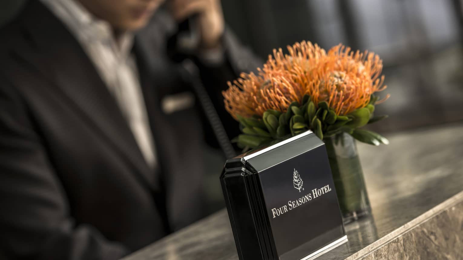 Close-up of Four Seasons Hotel concierge desk, orange flowers in vase, staff on phone