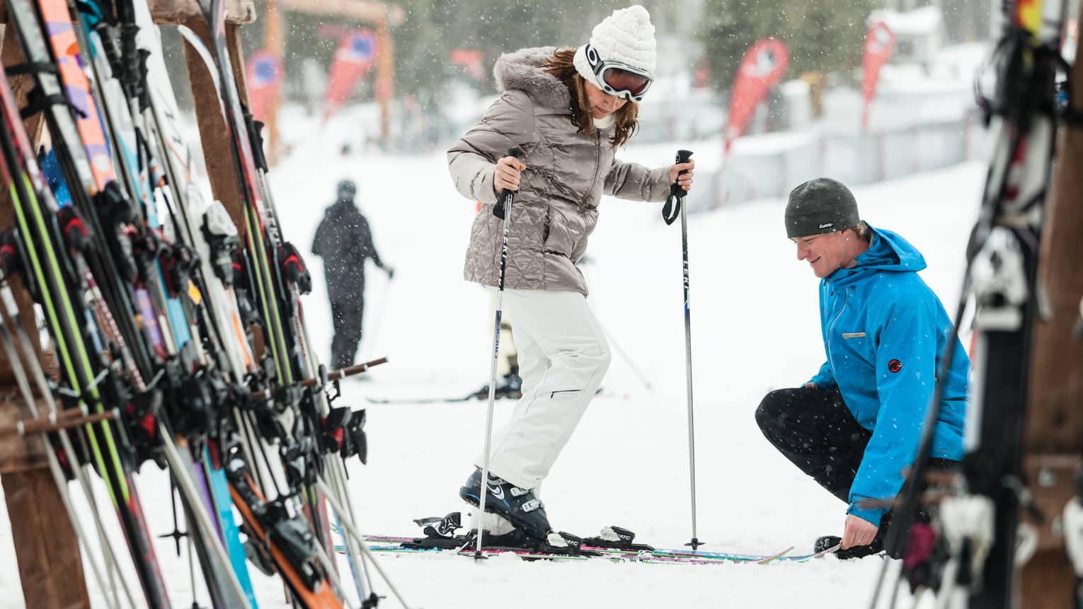 Ski concierge kneels down by woman trying on skis in front of rack