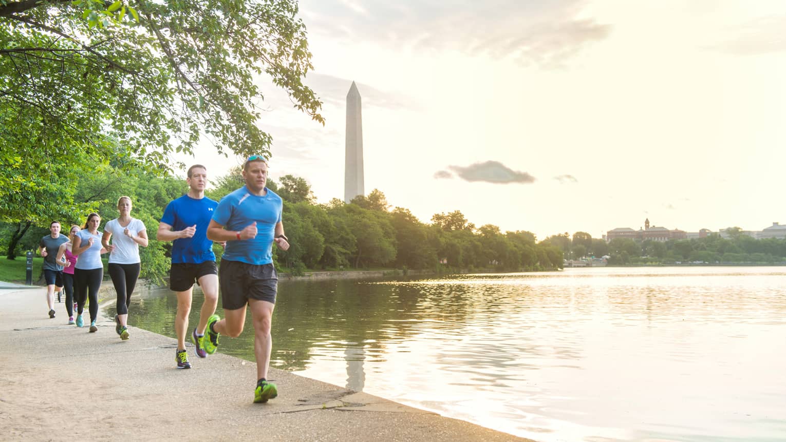 Group of men and women jog down path near water, Washington Monument in background