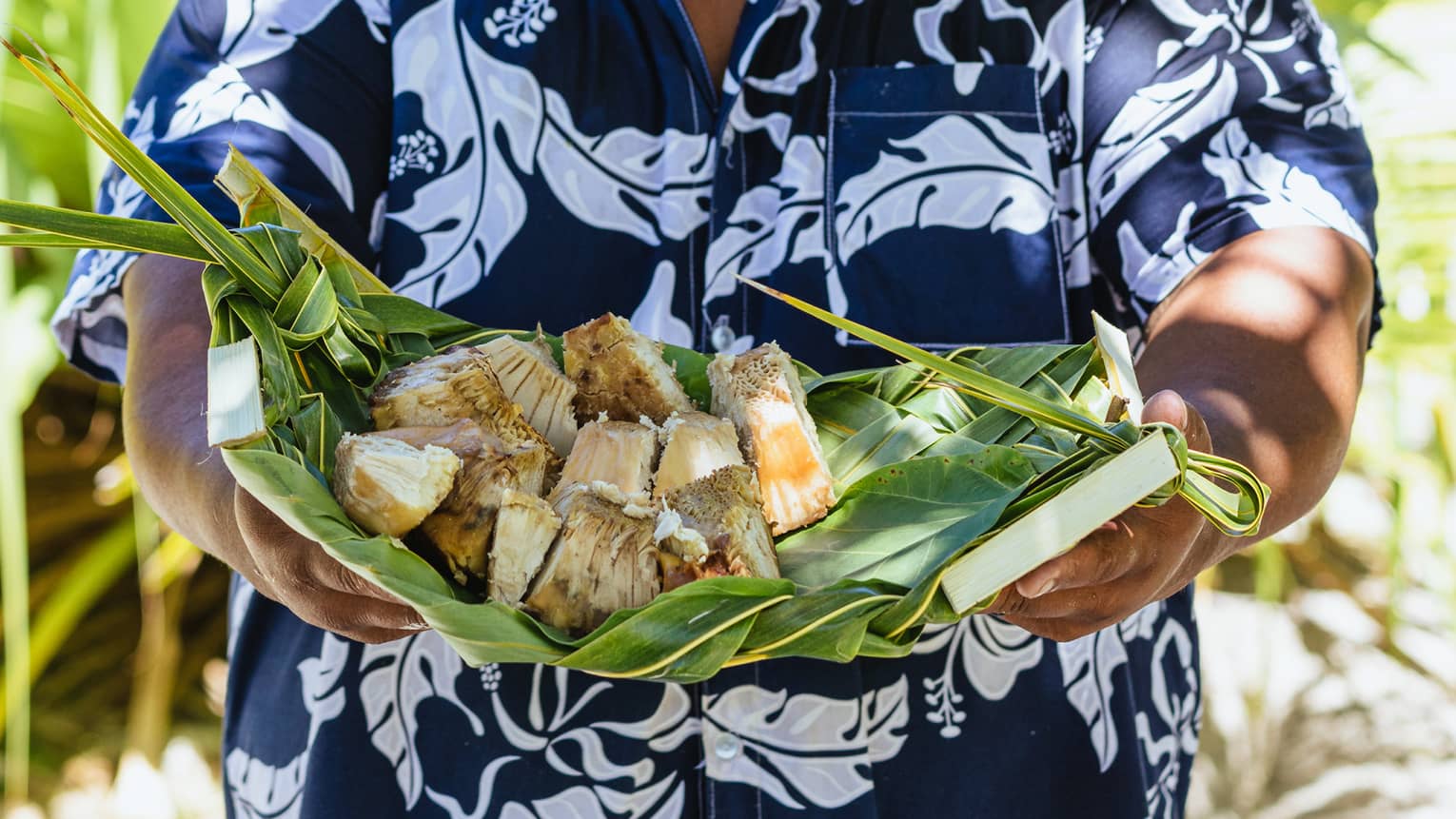 Palm leaves tied together to make a tray, on it rests several pieces of cooked breadfruit.
