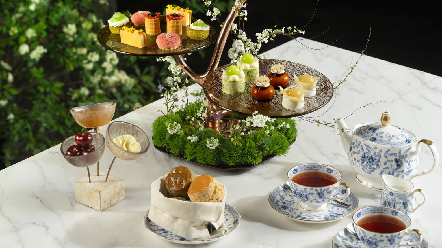 Tea and cakes on a table surrounded by greenery