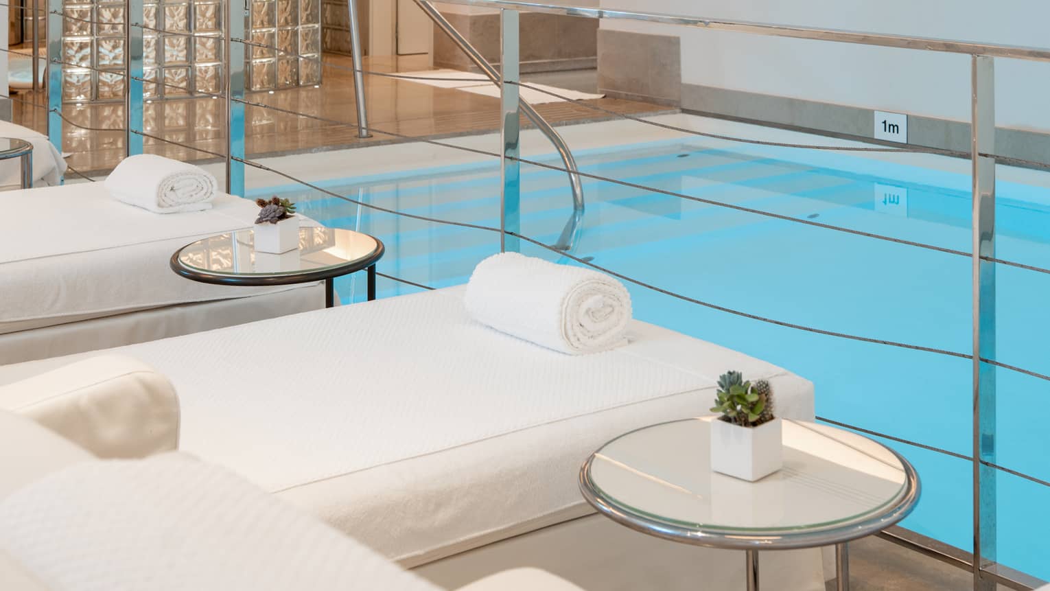 A spacious, well-lit indoor pool area with comfortable poolside spa treatment tables
