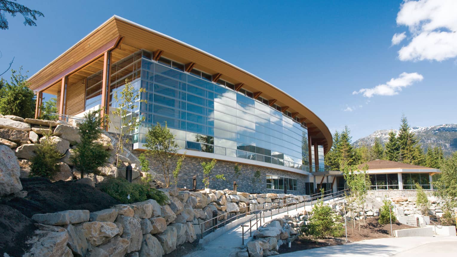 Exterior of Squamish Lil'Wat Cultural Centre with floor to ceiling windows, wooden roof, stone walls