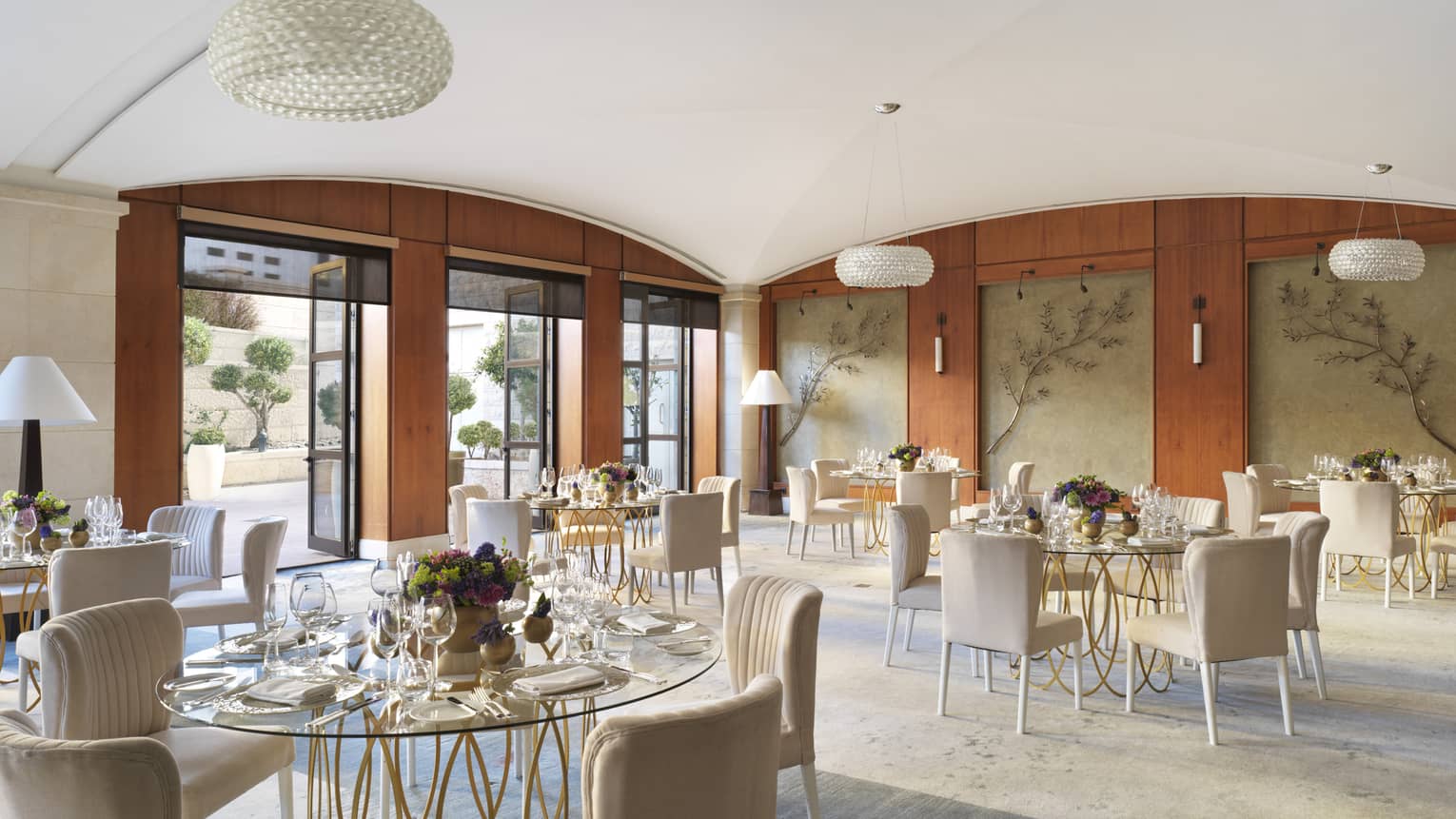 A large cafe with leaf decor on the walls, and several glass tables surrounded by cream coloured chairs. 