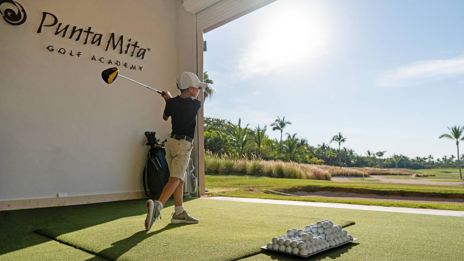 A young child practicing golf in a driving range.