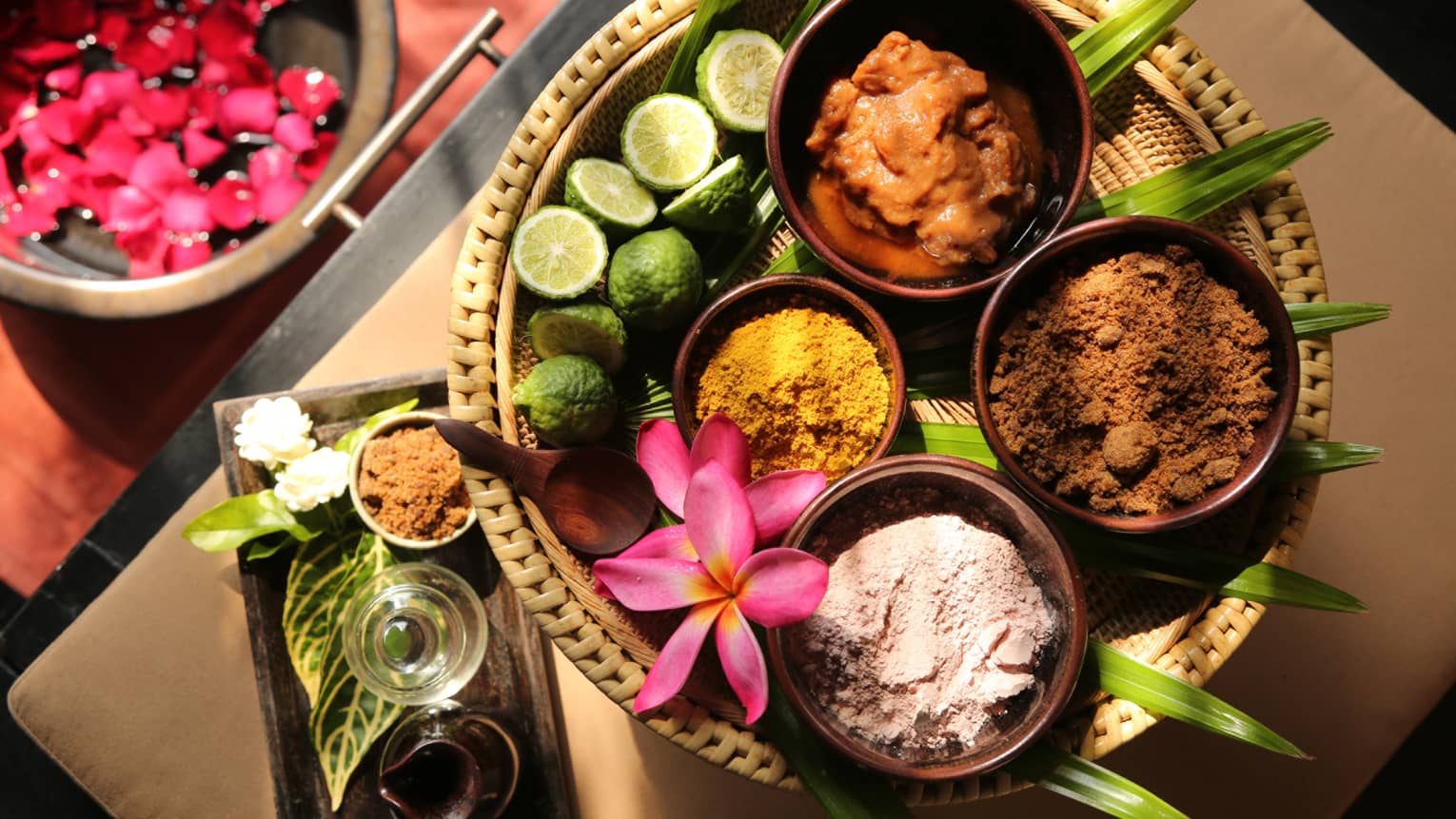 Assorted natural spa ingredients in bowls with lime, assorted spices and flower on a woven tray