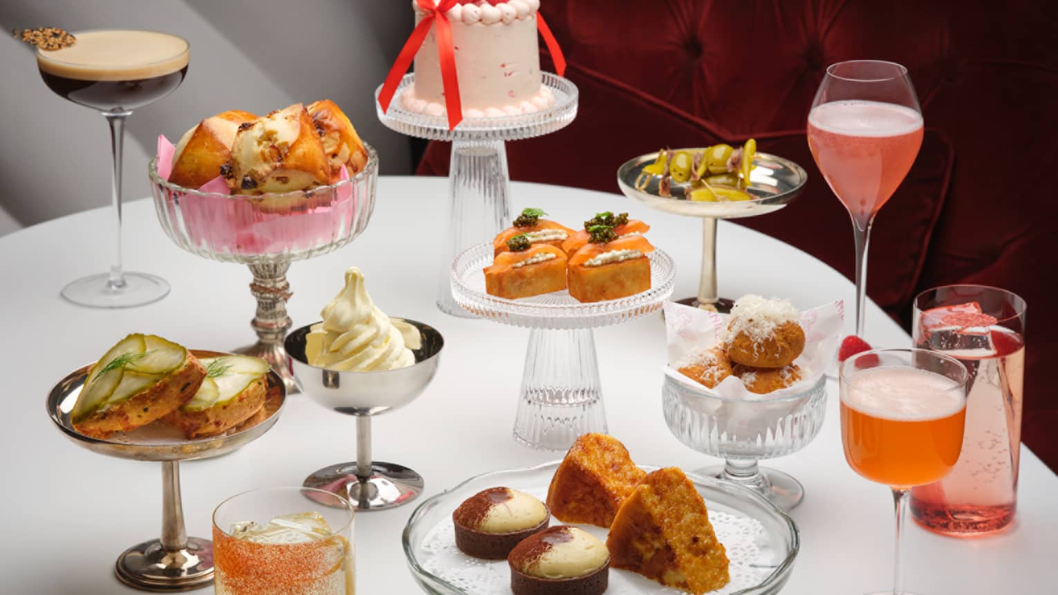 An assortment of colourful small bites and drinks on various stands, plates and glasses on a white table top