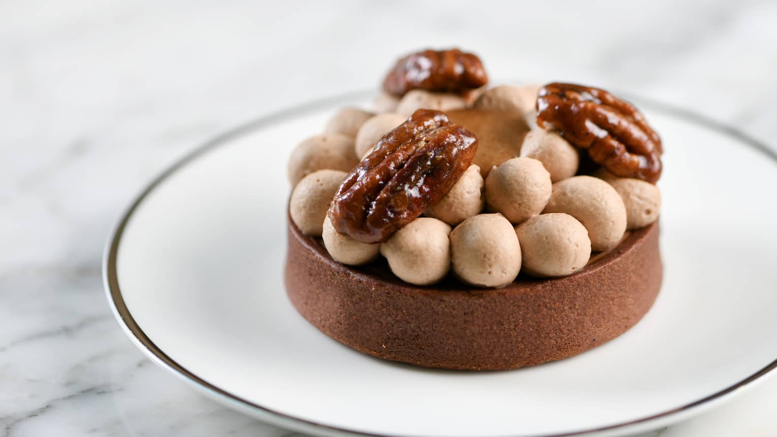 Round pecan tart topped with dollops of cream and three candied pecans