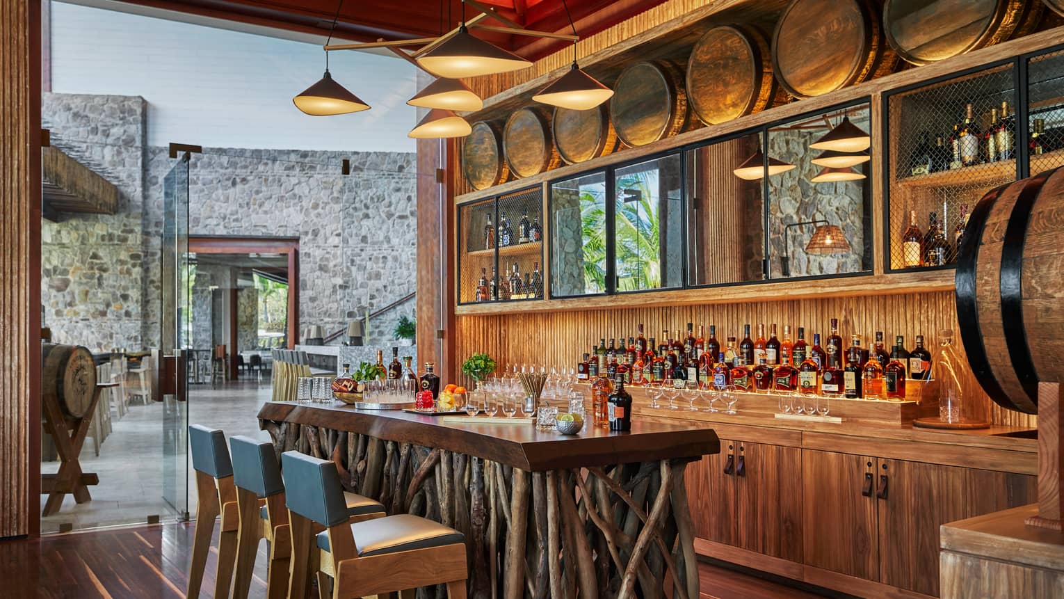 Modern chandelier above rustic wood tasting bar made from sticks, blue chairs, liquor display, barrel