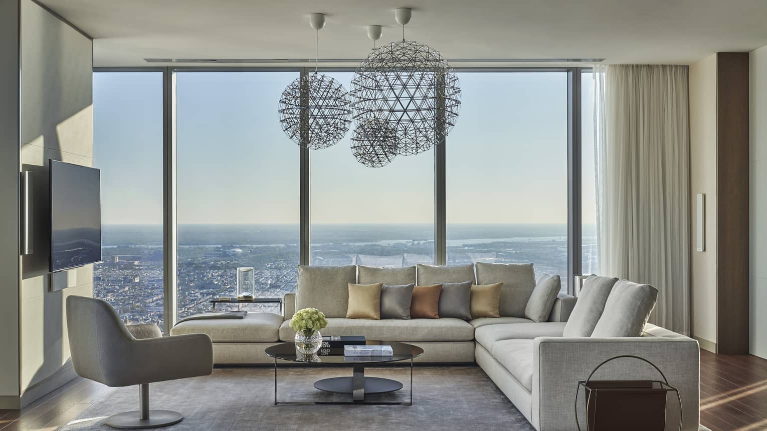 Living room with white l-shaped sofa, modern arm chair, three hanging light fixtures, wall of windows