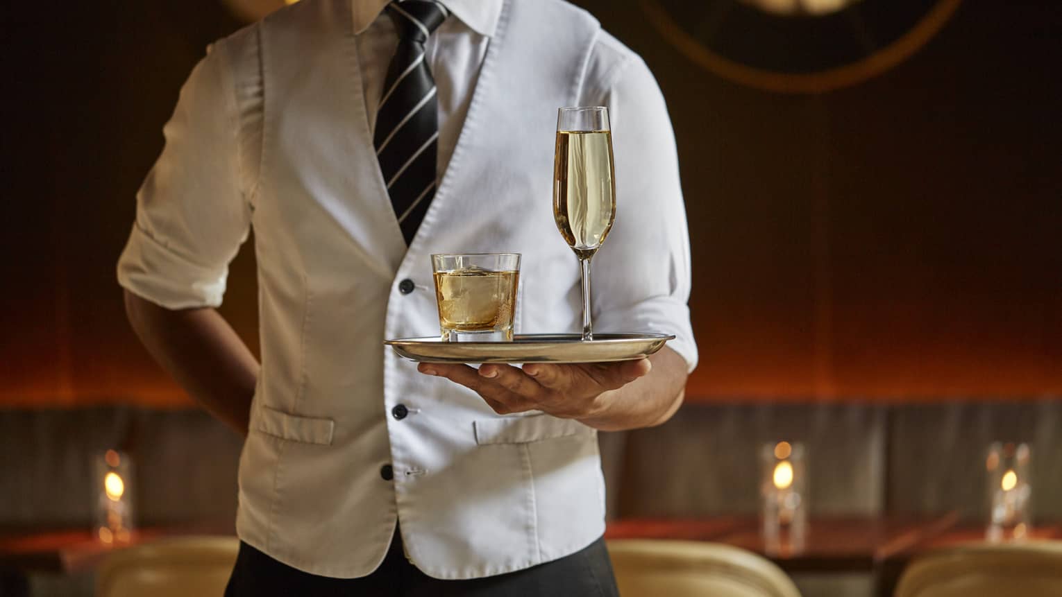 Server wearing a white vest holds tray of cocktails in an upscale lounge