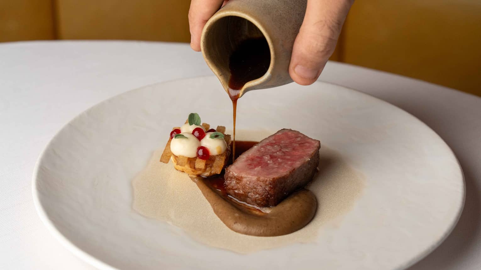 A round white plate holds a piece of cooked meat with garnishes and a sauce
