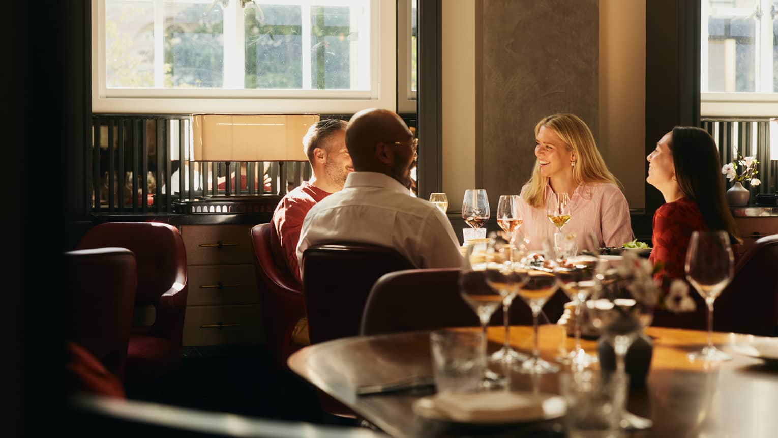 People sitting around a table, enjoying a meal in an indoor dining space. The table is next to a window that is letting in bright natural light.