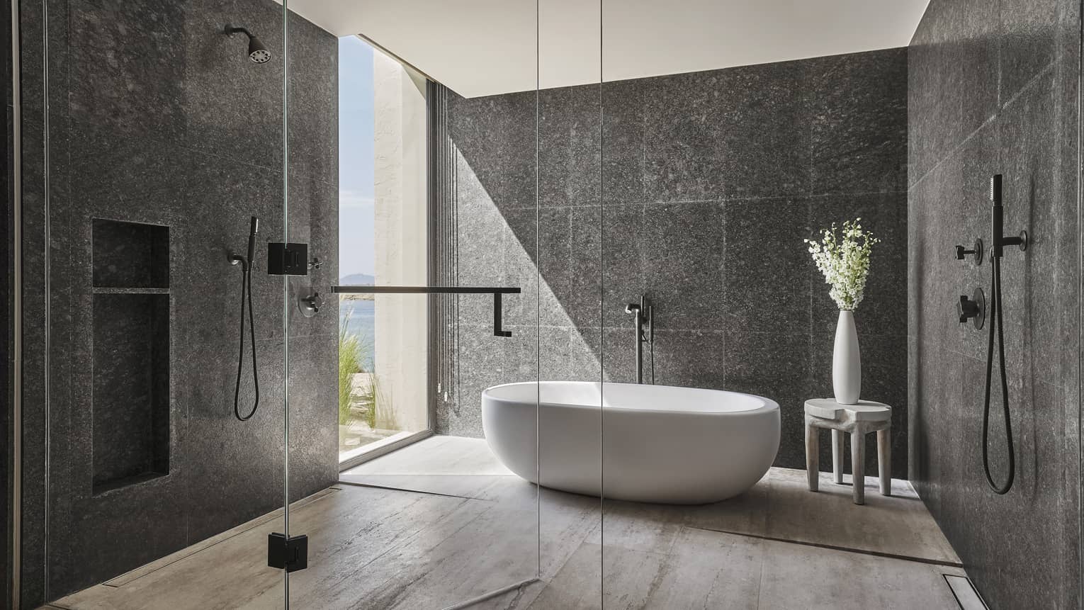 Two Bedroom Sunrise Suite bathroom with large soaking tub inside marble-walled enclosed glass shower, floor-to-ceiling window with ocean views