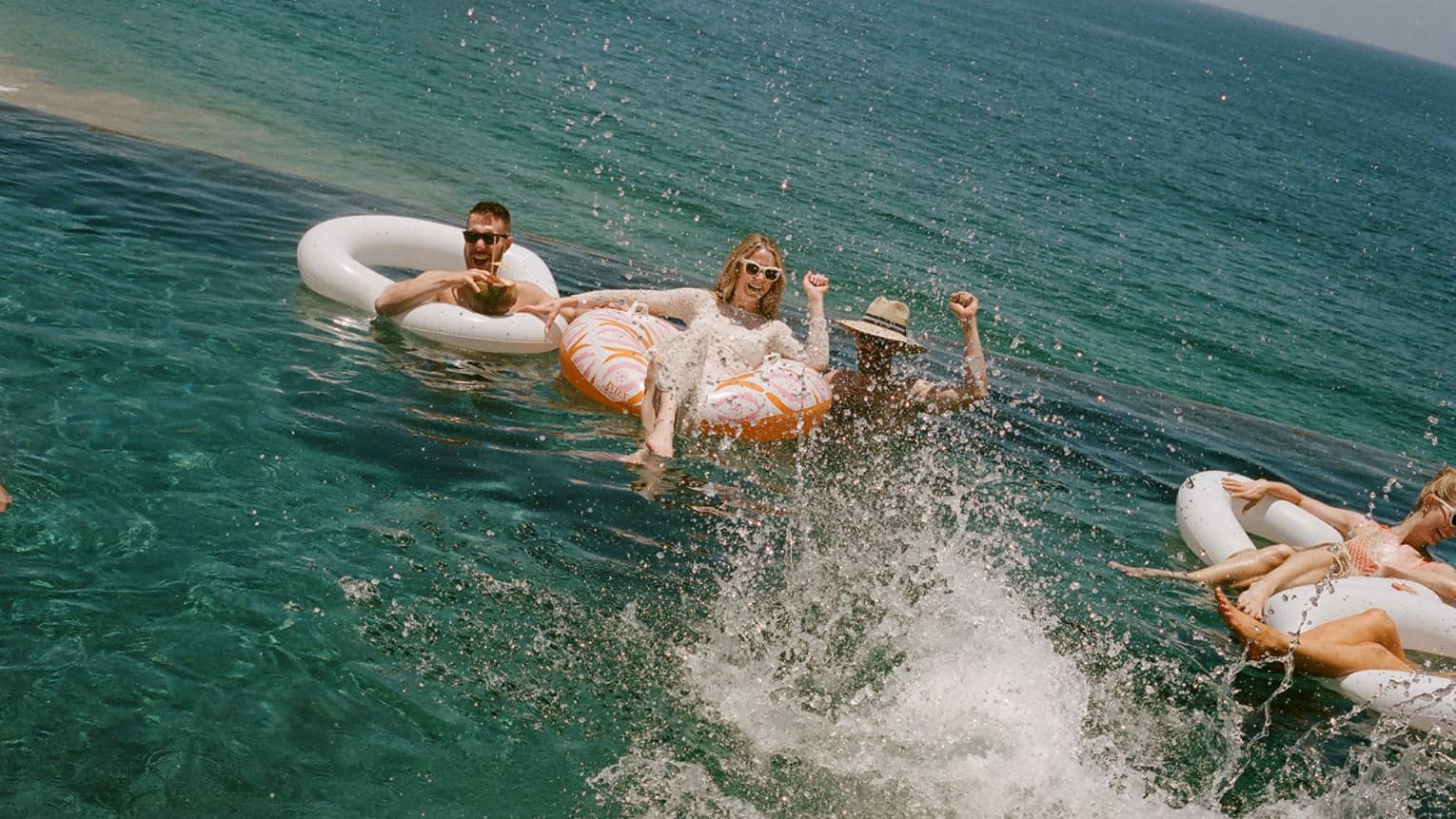 Several people floating and splashing in the ocean in inflatable tube floats