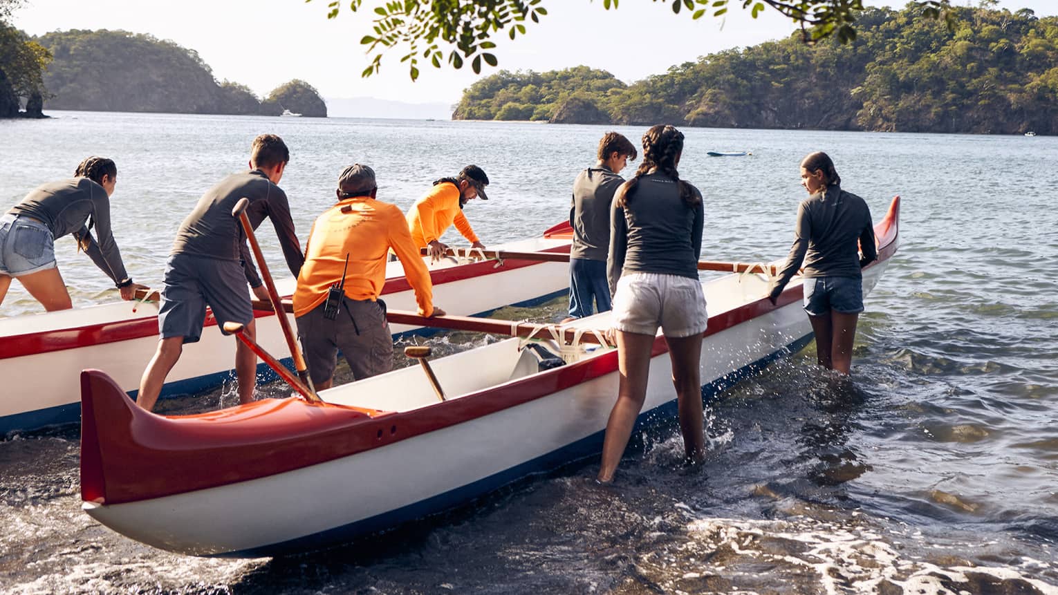 A group of people pushing canoes out onto water.