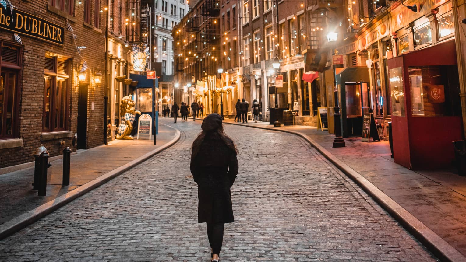 A woman in a winter coat walking down a street with many lights.