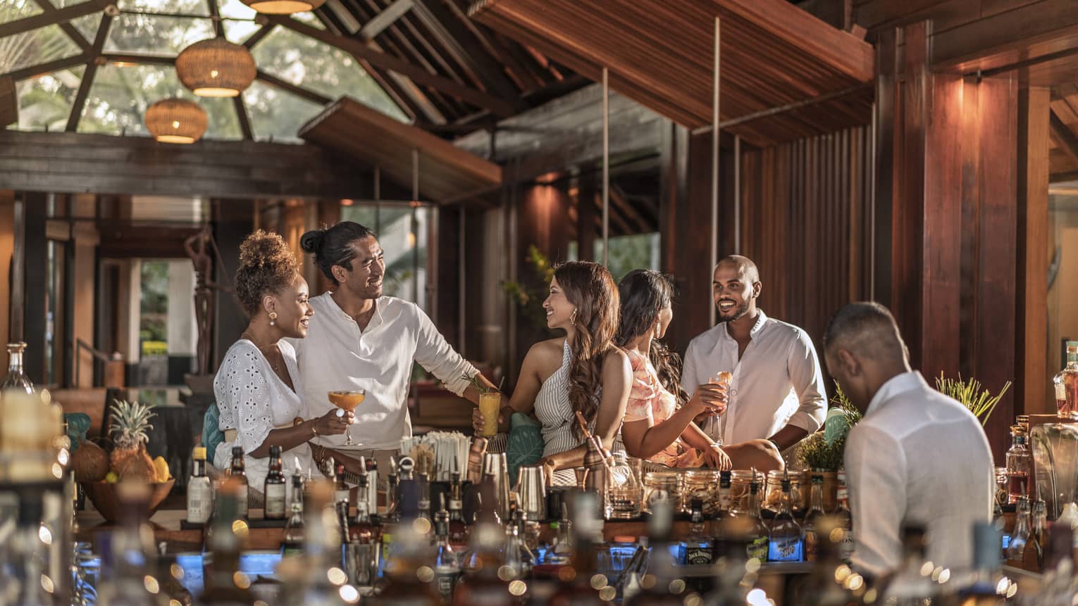 Five friends standing and talking over drinks by a stocked bar