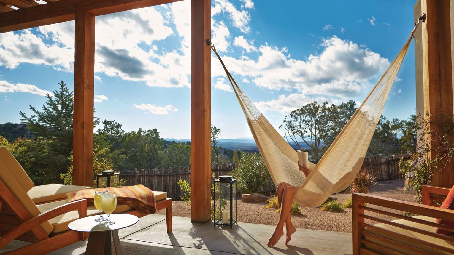 Woman lounges, reads book in hammock under wood pergola on patio