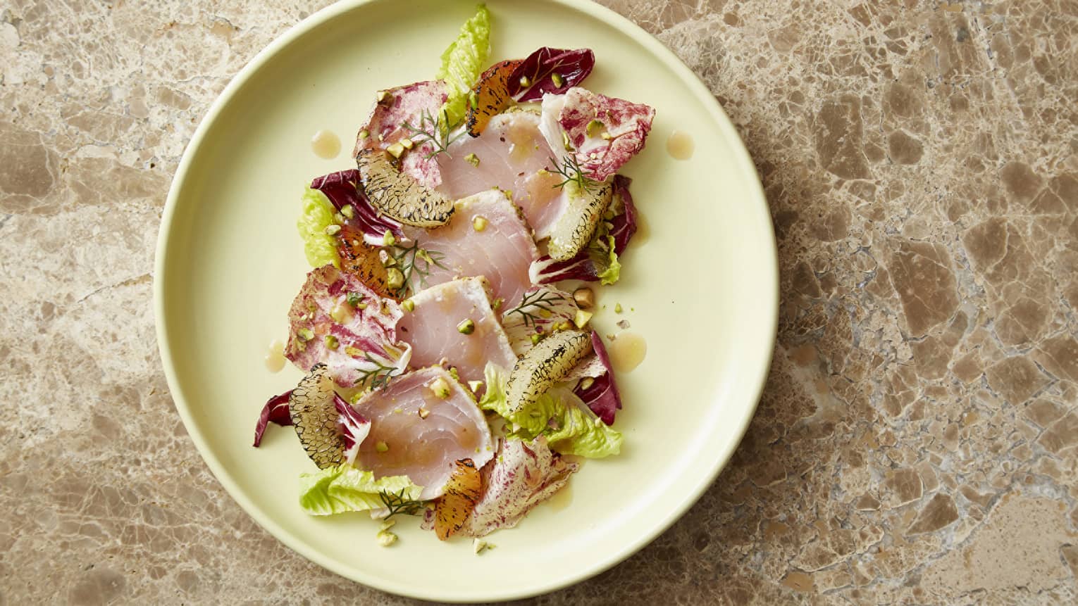 Swordfish, citrus, pistachio and radicchio on a light yellow plate