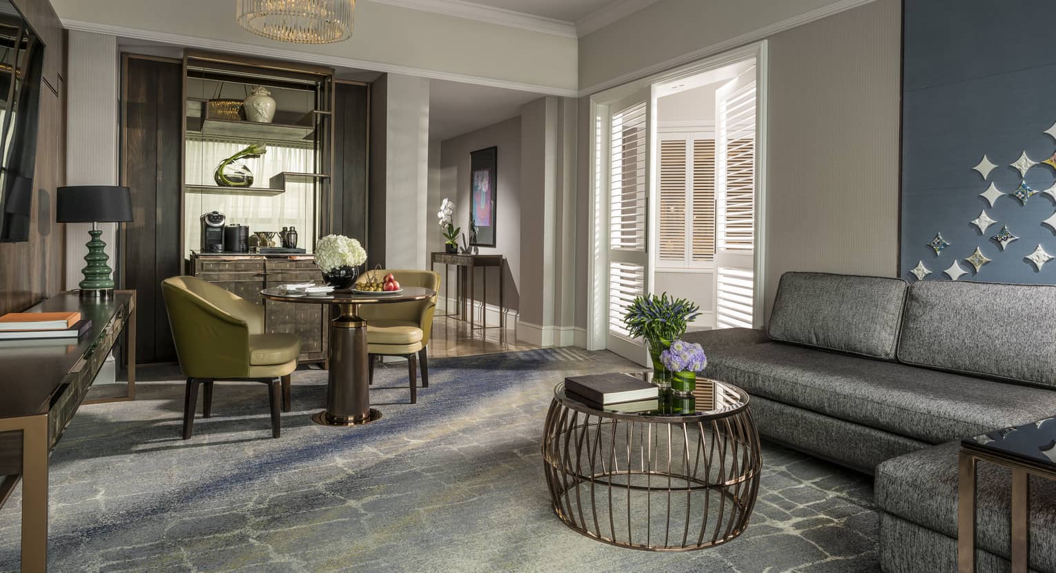 Gold dining chairs around small dining table by brass wire table, L-shaped grey sofa