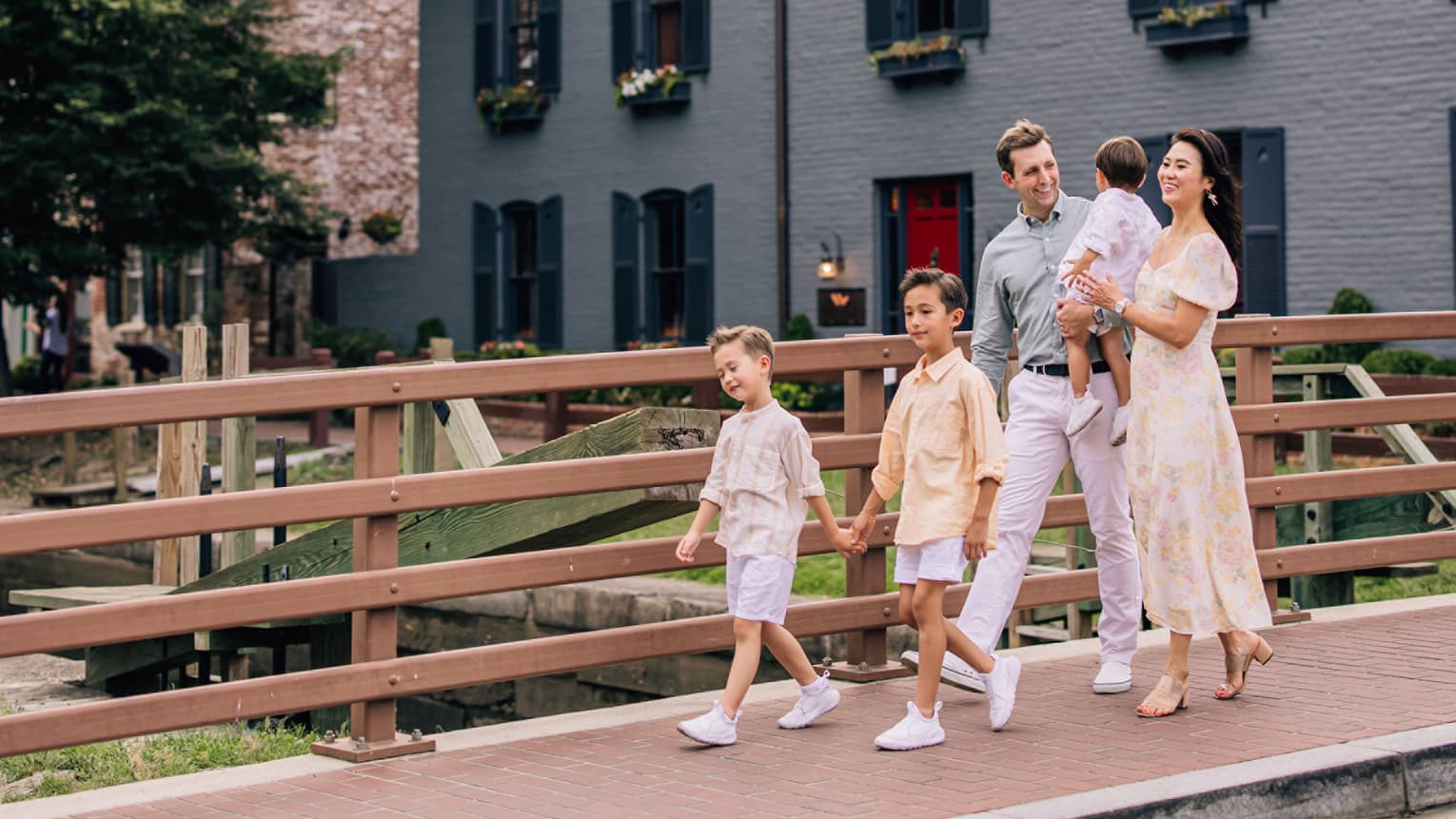 Man, woman, and three young children walk along a sidewalk over a bridge