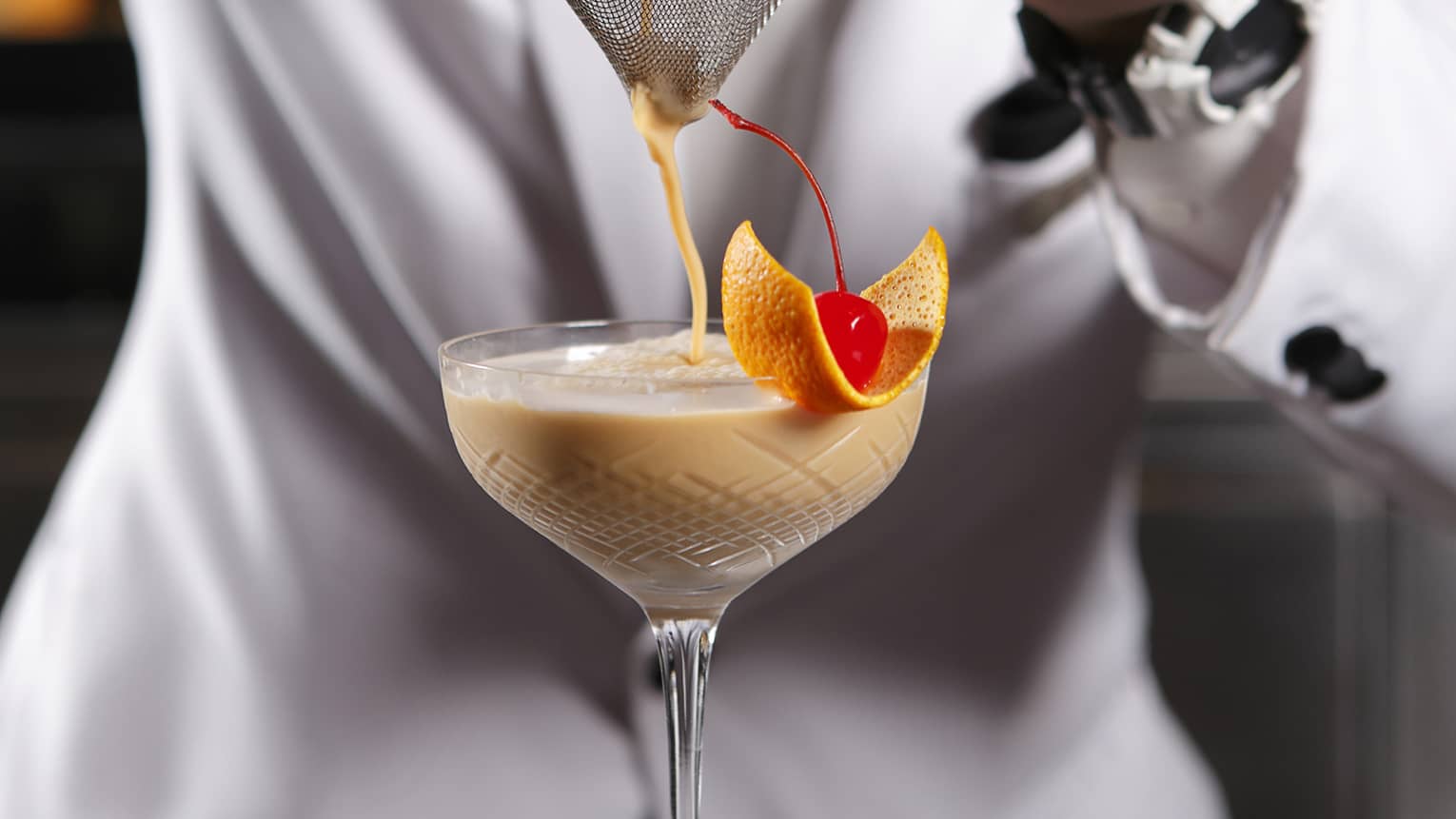 Mixologist pours cocktail into long-stemmed glass at bar 