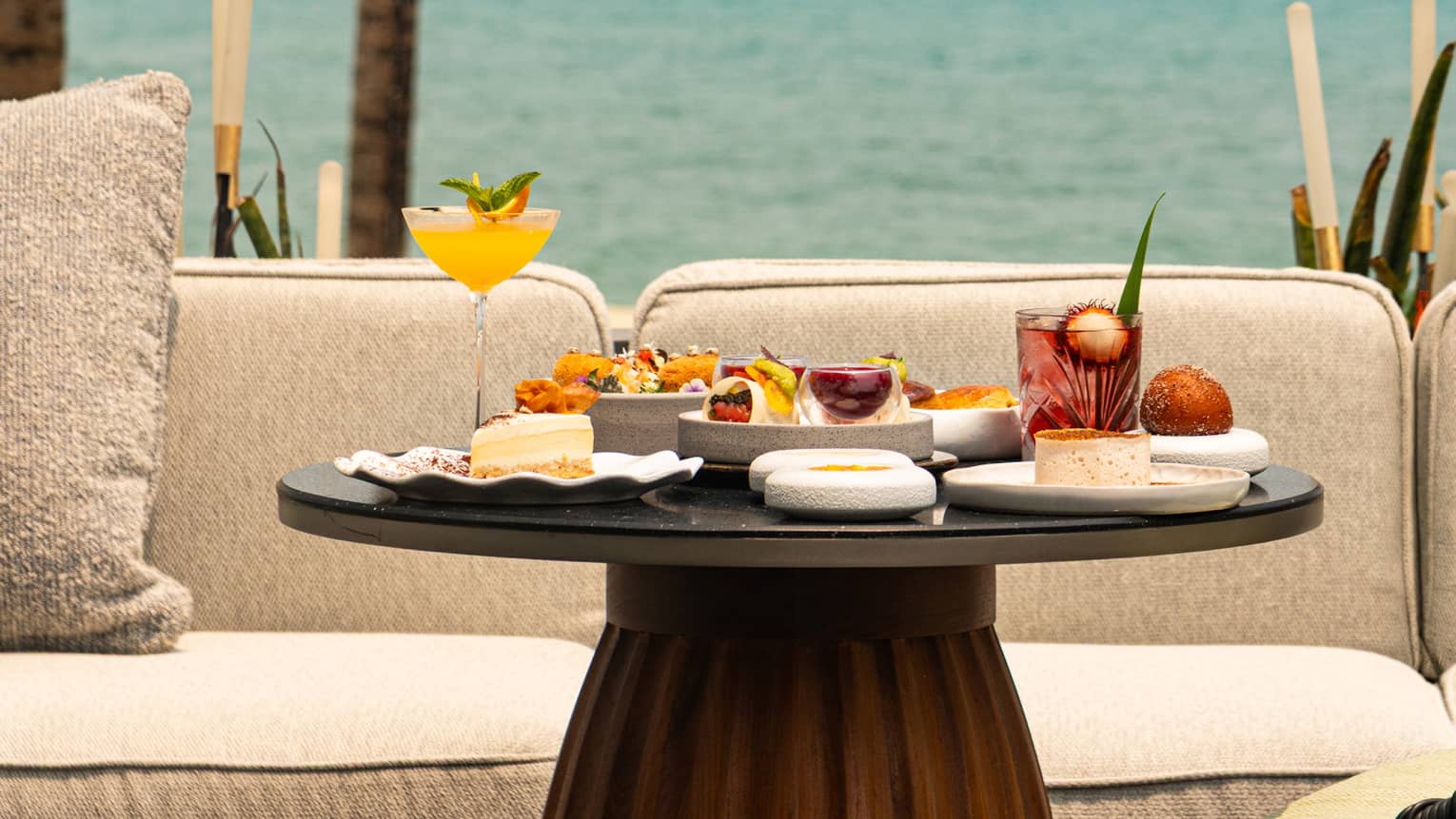 Round table set for afternoon tea in front of cream outdoor sofa, overlooking the sea