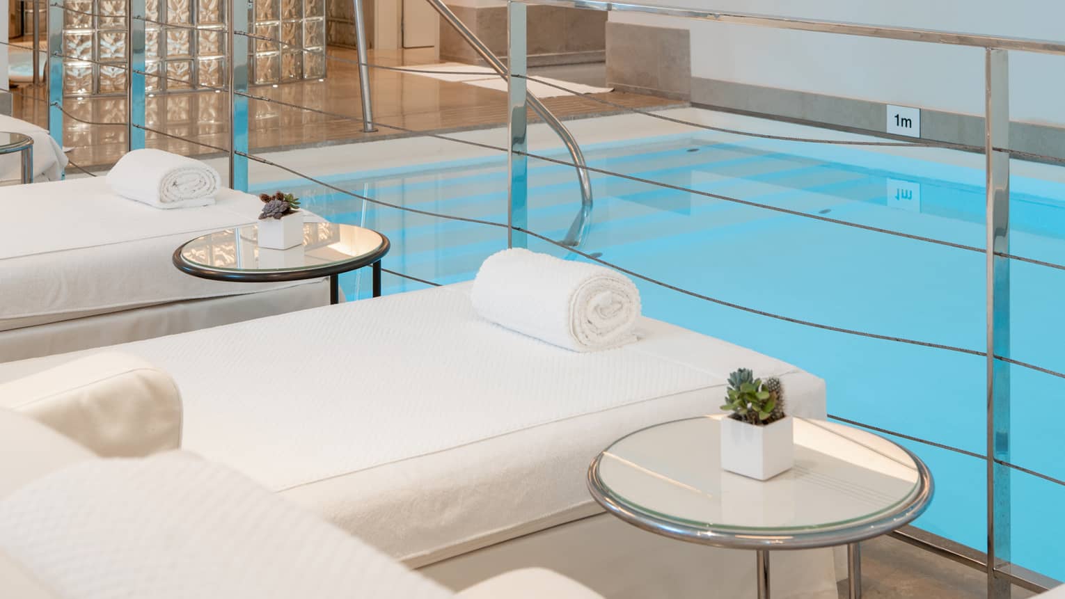 A spacious, well-lit indoor pool area with comfortable poolside spa treatment tables