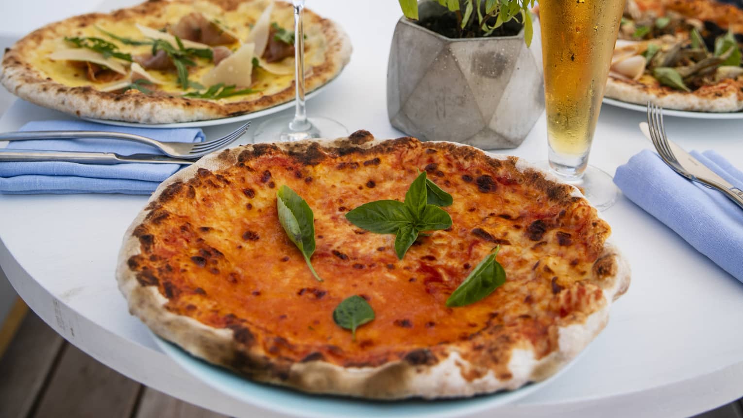 A table set with a glass of rose and a pilsner of beer with craft pizzas on it overlooking the beach at Four Seasons Maldives - Landa
