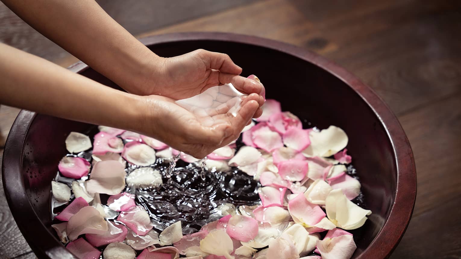 Pari fo hands clasped together brings water up from a large bowl filled with pink and white rose petals