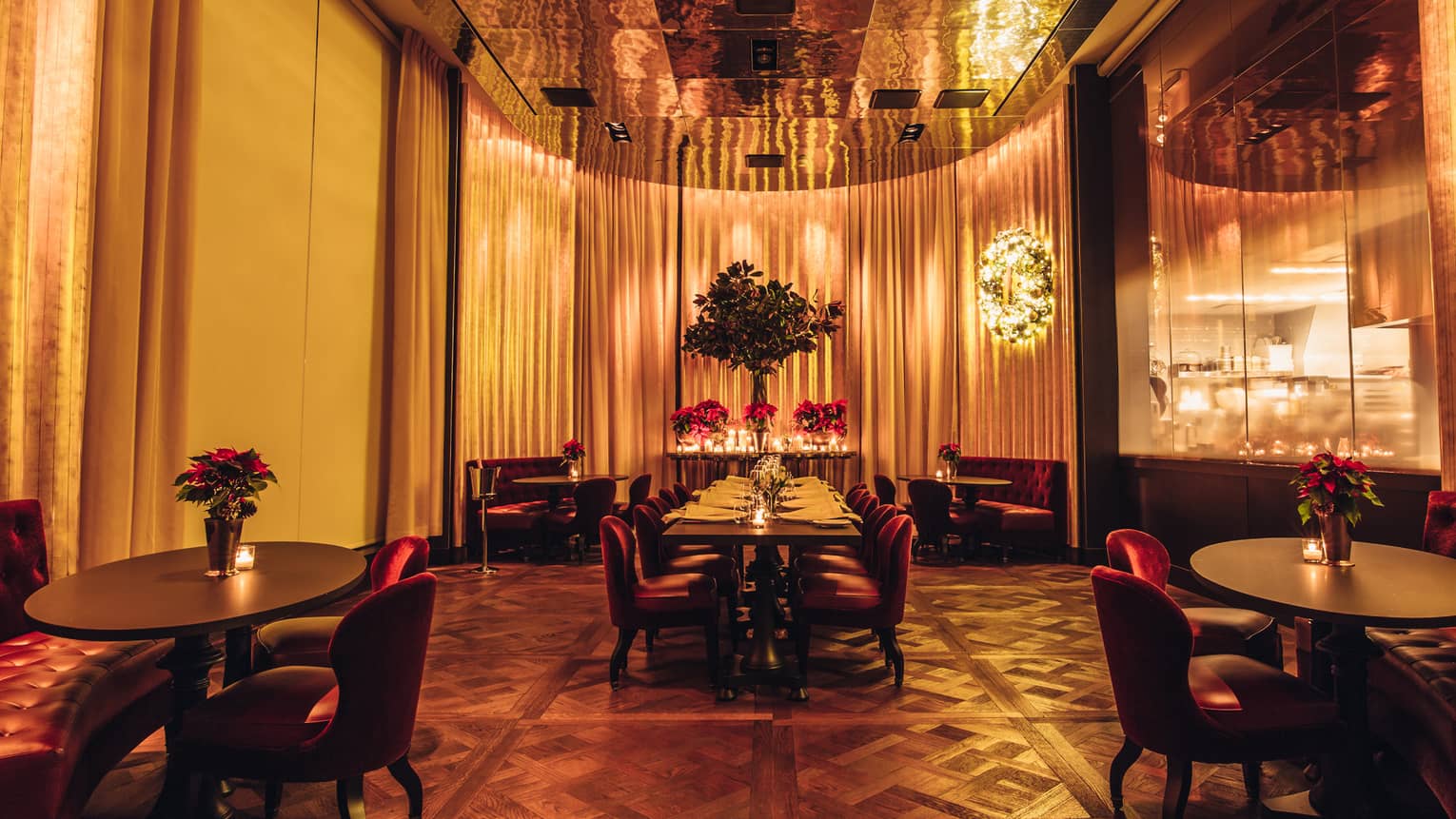 Candle-lit dining area with tables, red velvet lounge chairs, brass accents, tall mirrors and curtains