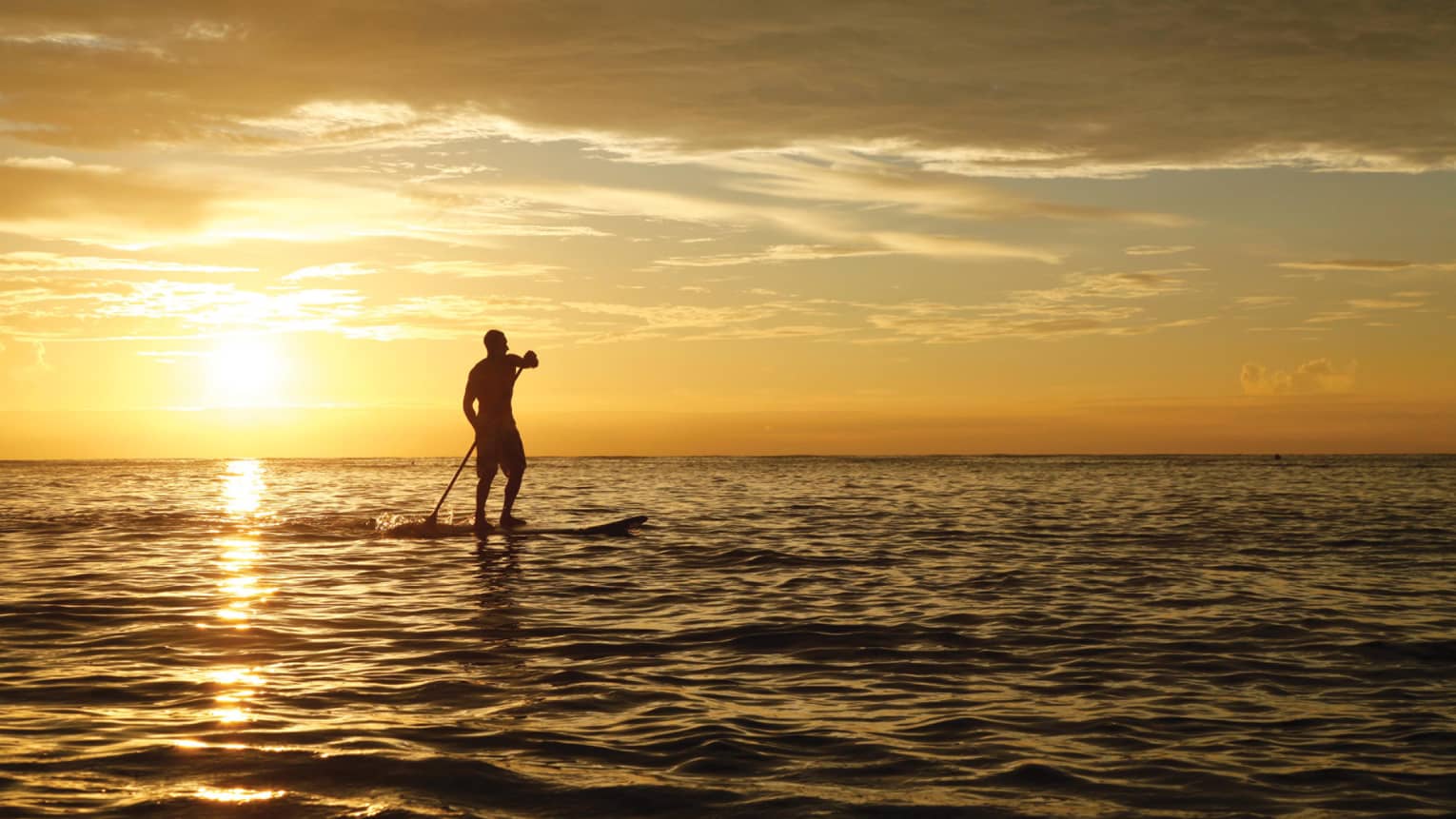 Silhouette of person with paddle on stand-up paddleboard on ocean, orange sunset