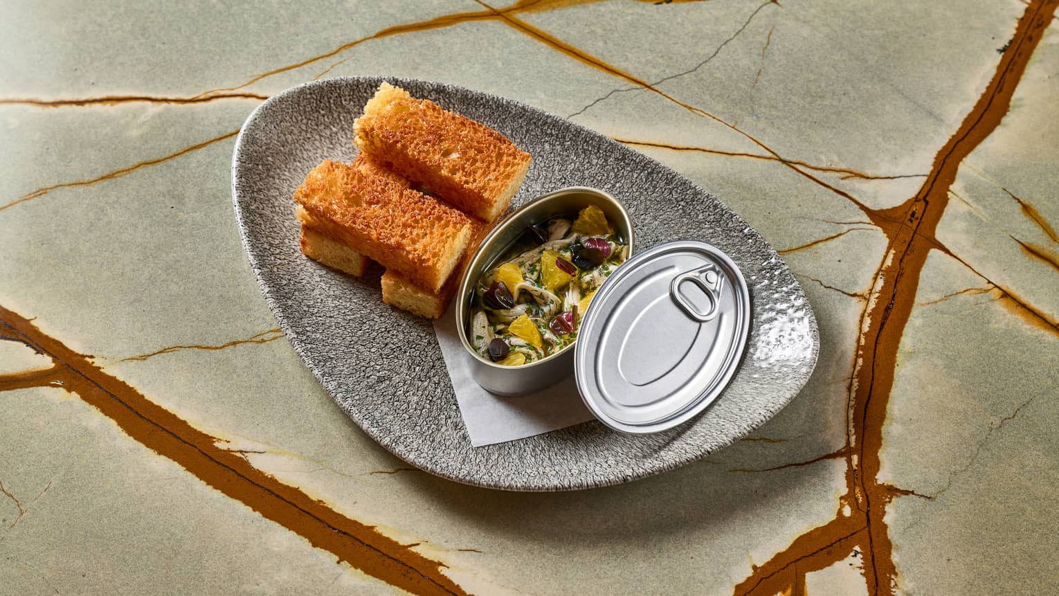 Anchovies served in a tin with toasted brioche on the side