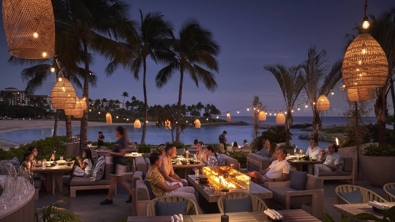 Guests dining at dusk on lagoon-side restaurant patio draped in lanterns