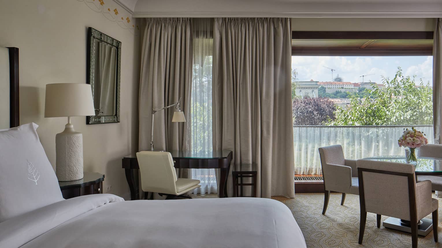 A room with a bed, desk and chair, table and chairs and large window.