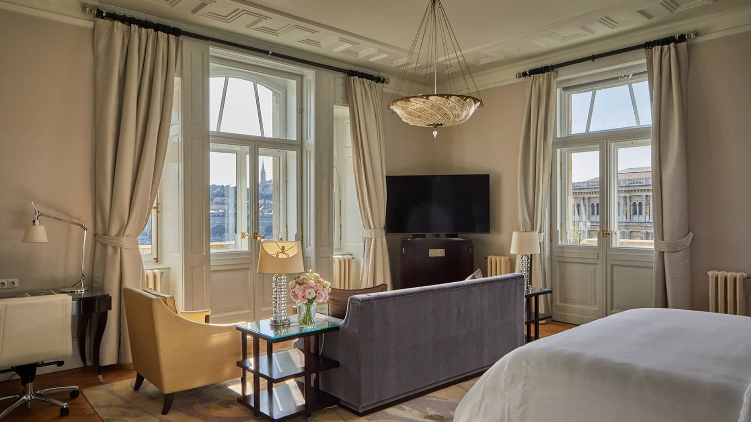 A room with sofa, bed, chair, side table, two windows and a television.