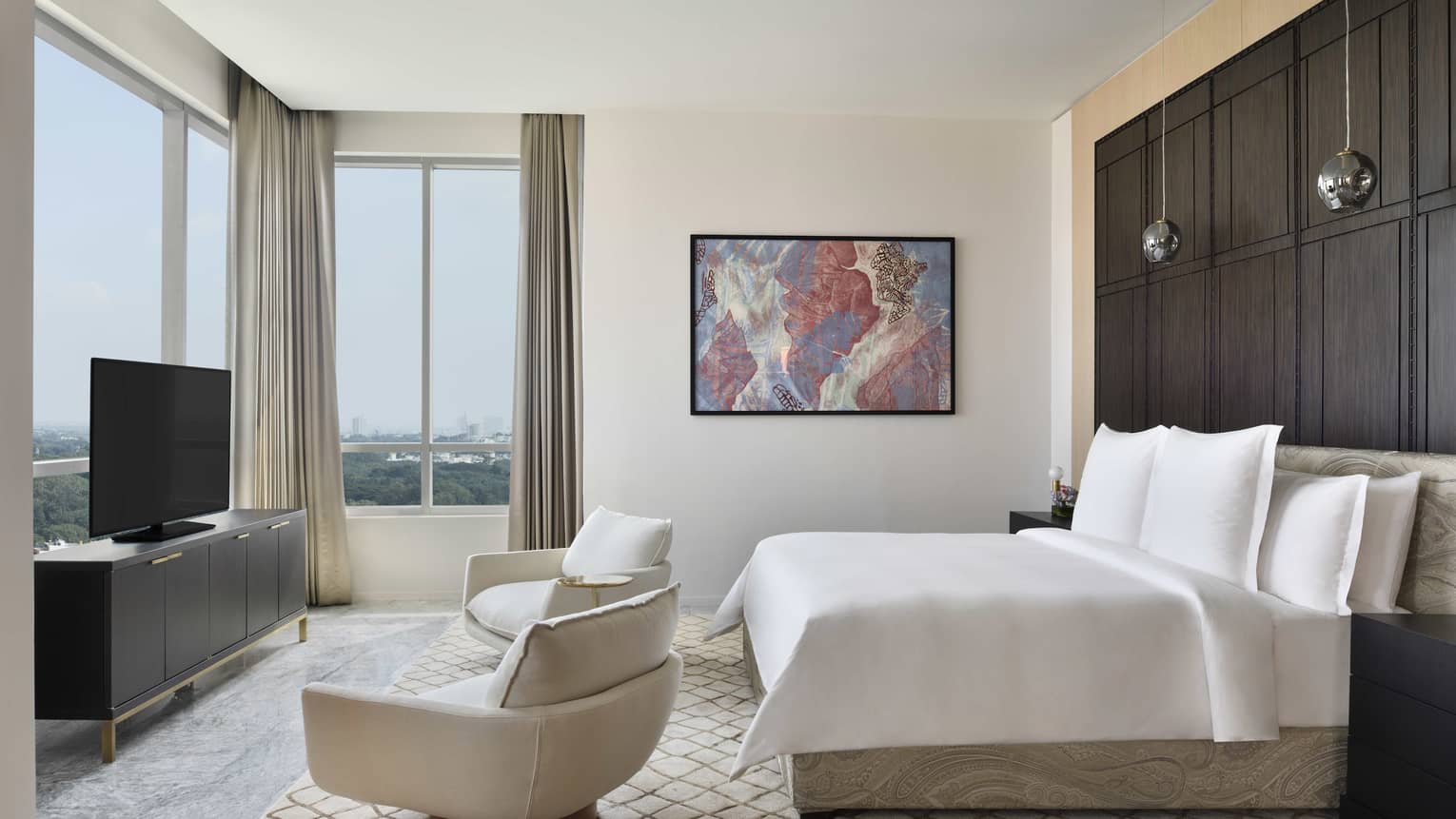 Bedroom with king bed, two arm chairs, TV and windows