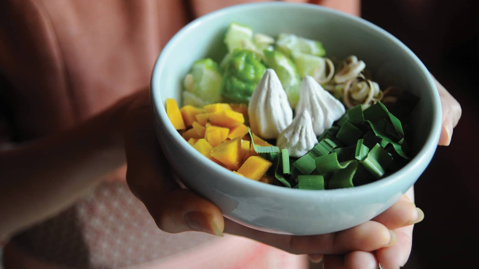 Woman holds white bowl with diced plants and fruits spa ingredients