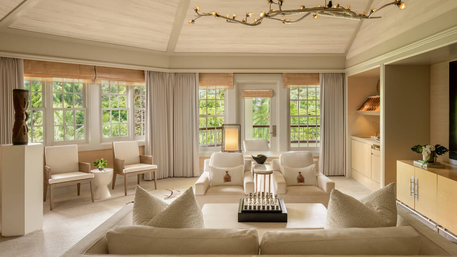 Light-filled living area of a luxury resort suite with vaulted ceiling, white and beige upholstery, and garden views