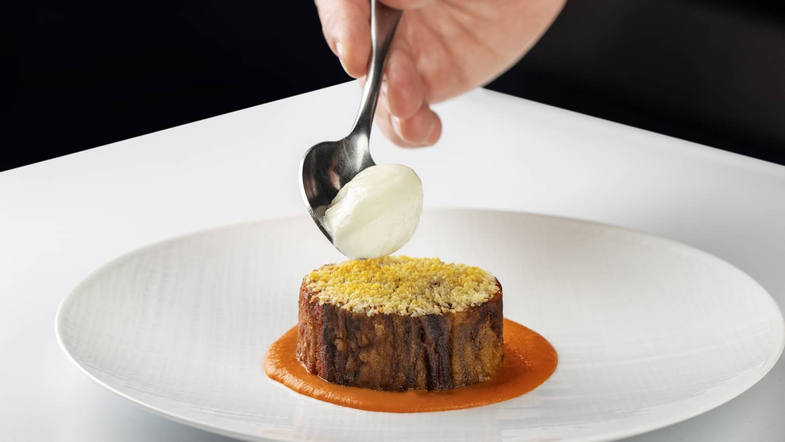 Chef?s hand places dollop of cr�me fra�che onto dish on round white plate